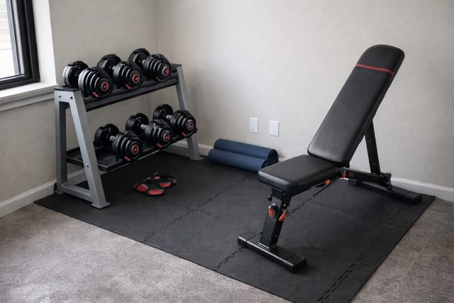 Home gym setup showing bench and adjustable dumbbells in compact workout space