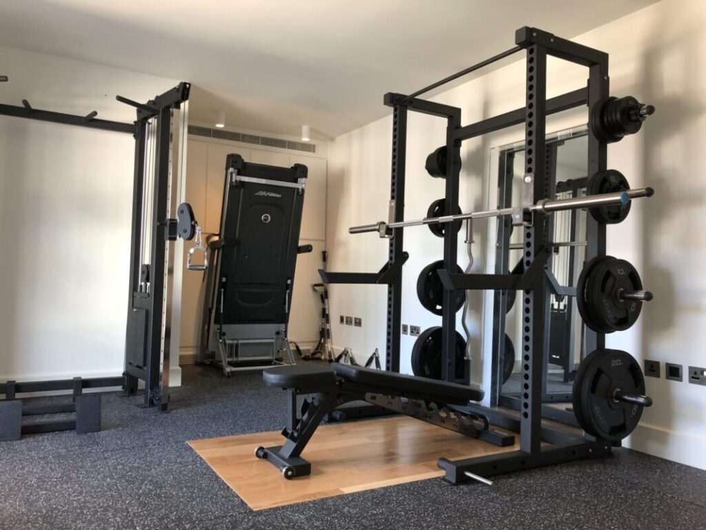 Adjustable weight bench inside a full home gym with power rack, barbell, weight plates, and cable machine