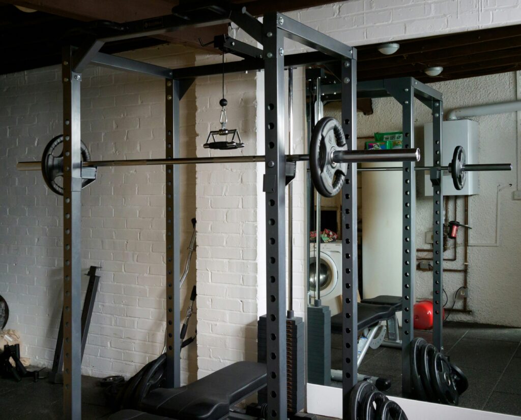Home gym equipment layout showing power rack, barbell, weight plates, and bench organized in a garage gym