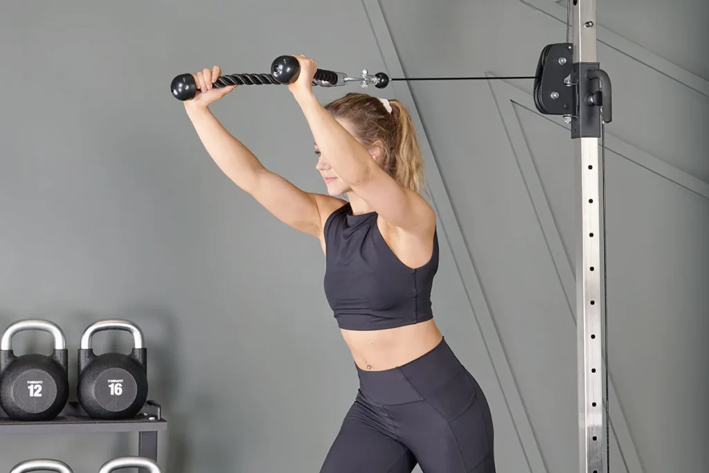 woman performing cable triceps pushdown exercise with rope attachment in home gym