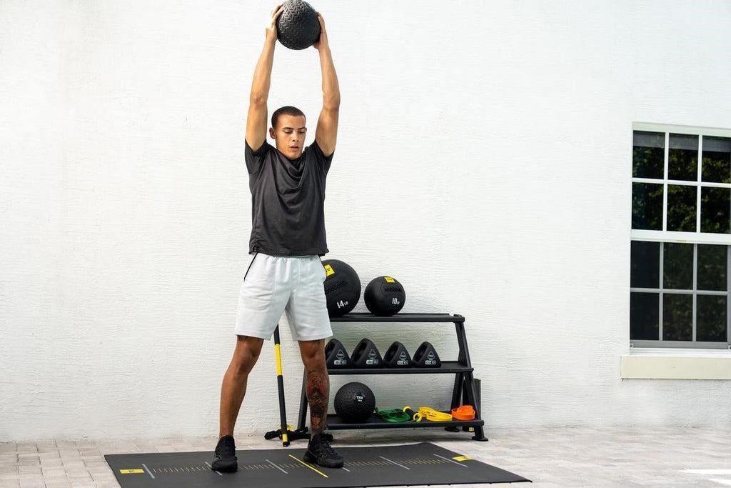 Athlete performing a medicine ball overhead movement in a home gym