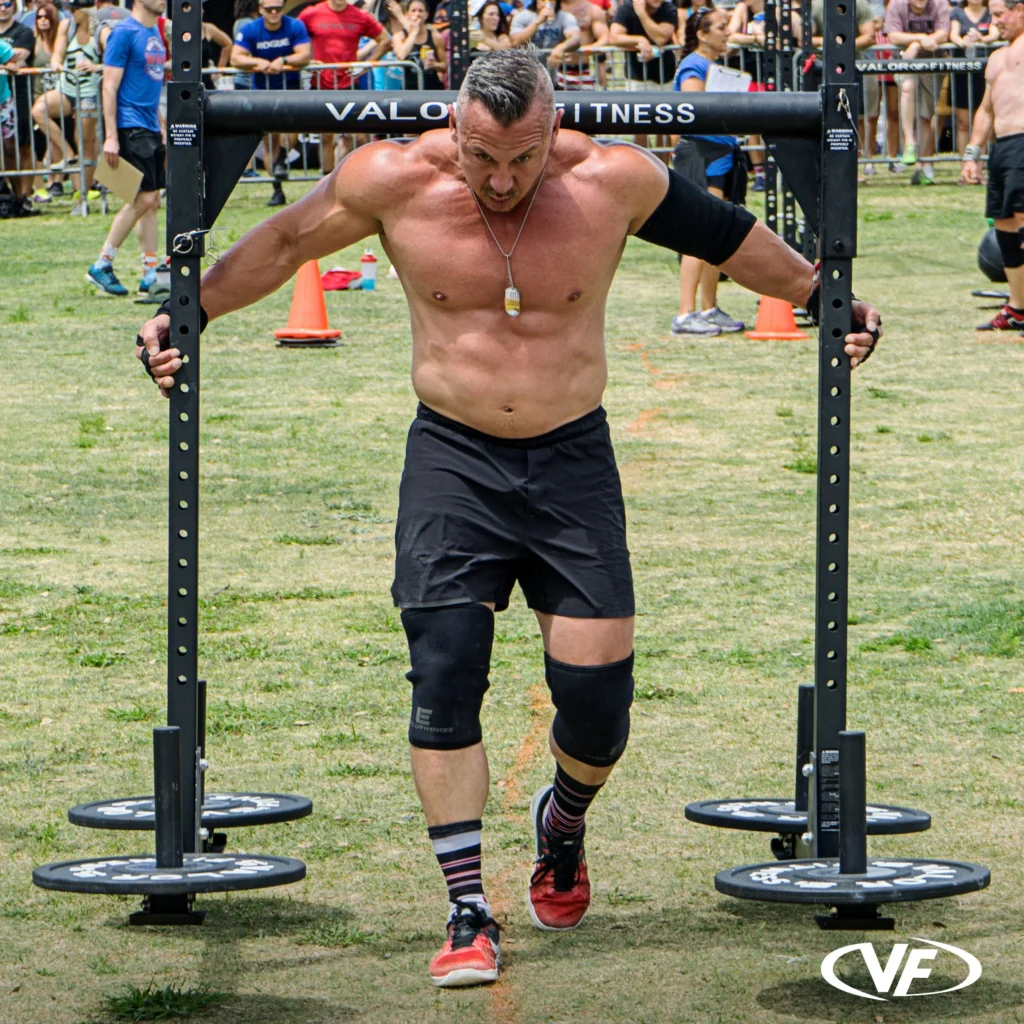 Athlete performing a heavy strongman yoke carry outdoors with a black plate-loaded yoke
